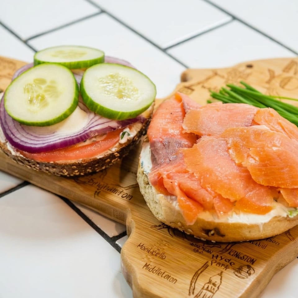 Open-faced bagels topped with smoked salmon, cream cheese, cucumber, red onion, chives, and capers on wooden serving boards.